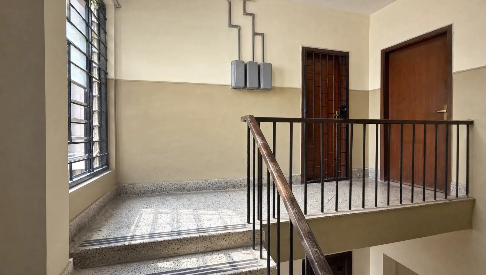 AI-generated illustration of a terrazzo stairwell landing in a Karachi apartment building with a grilled window and meter boxes.